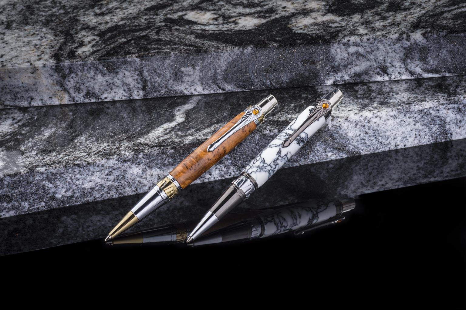 Two Art Deco pens arranged on veined stone above a reflective black surface